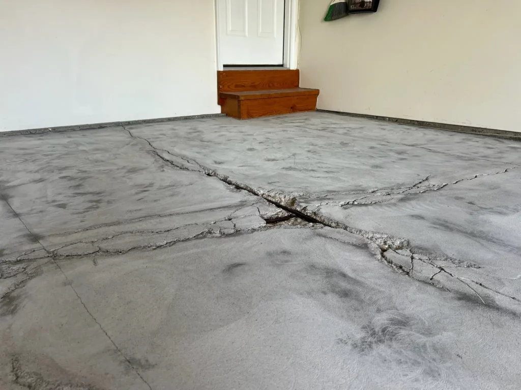 A garage floor in O’Fallon, Missouri, with exposed rebar due to deep cracks, highlighting the need for concrete restoration.